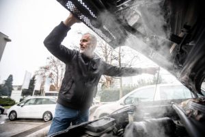 Steam Coming Out of Car Engine While Mature Man is Opening the Hood .