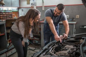 Young man car mechanic talking with woman customer at auto repair shop